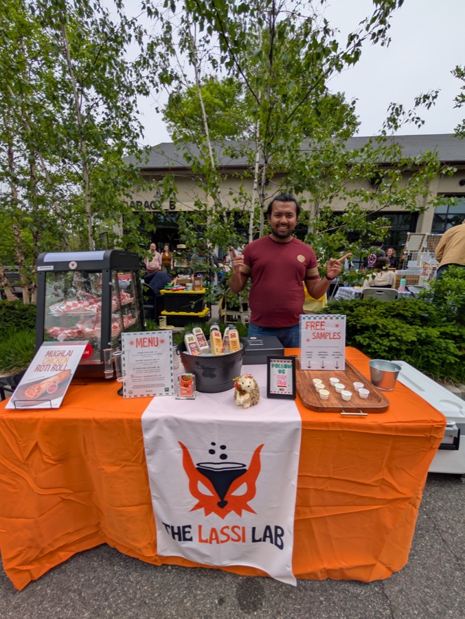 The Lassi Lab stall at Brighton Bazaar, bottles and a menu laid out on the orange counter