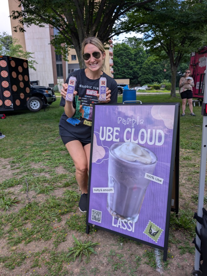 A customer holding two bottles beside the Purple Ube Cloud Lassi sign